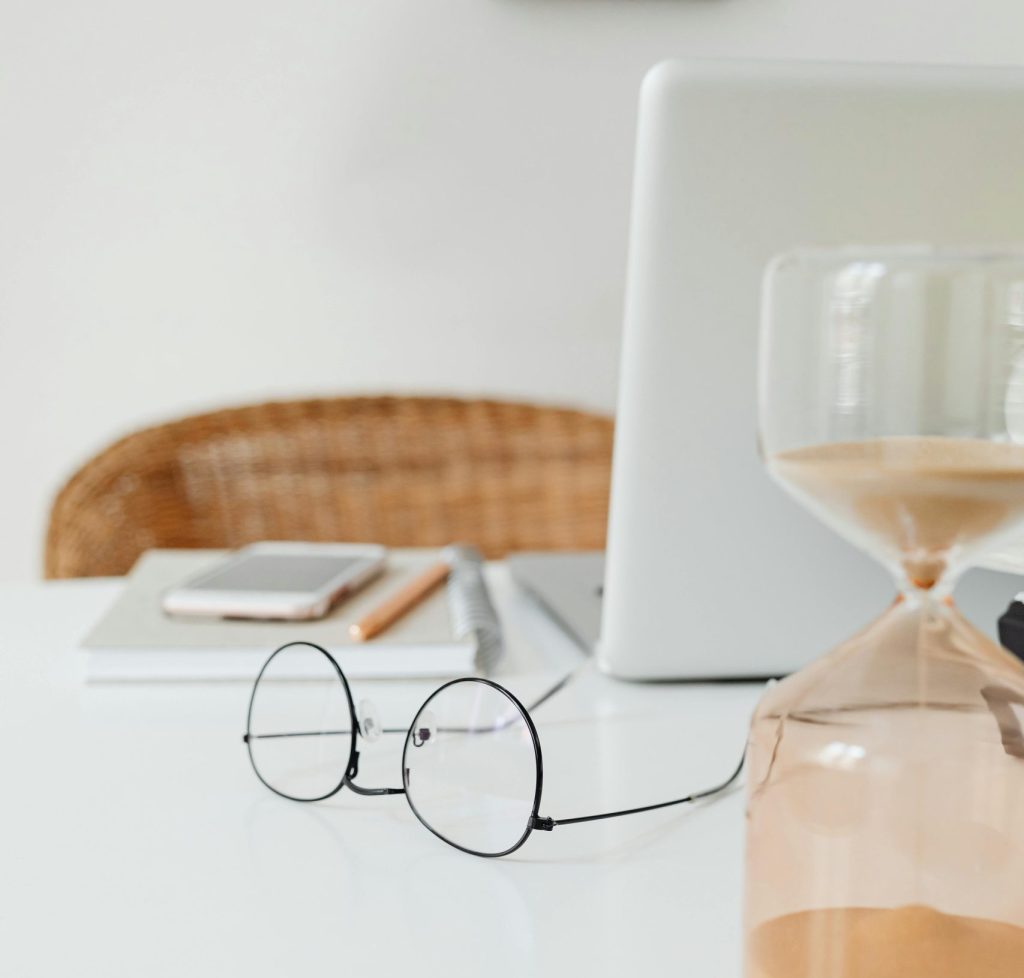 A clean and modern workspace featuring an hourglass and eyeglasses on a desk.